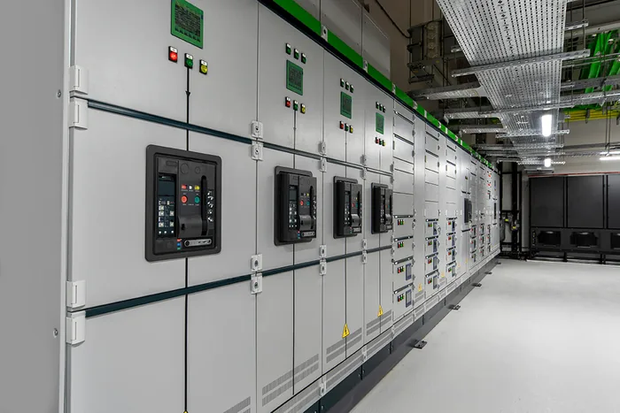 Sala de painéis elétricos industriais alinhados, com quadros de comando e infraestrutura de cabos no teto